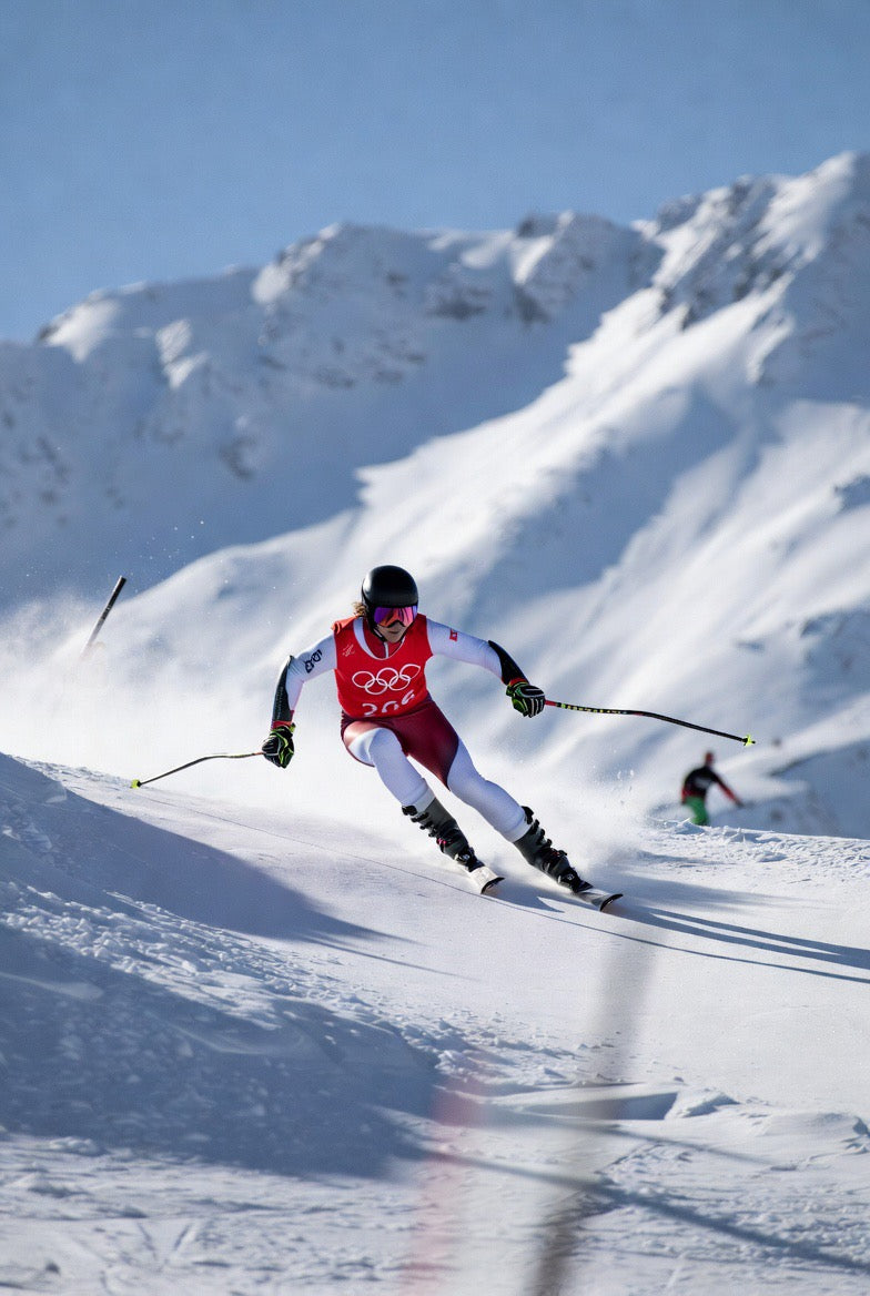 Olympic skier racing downhill on snowy mountain, wearing red suit and helmet