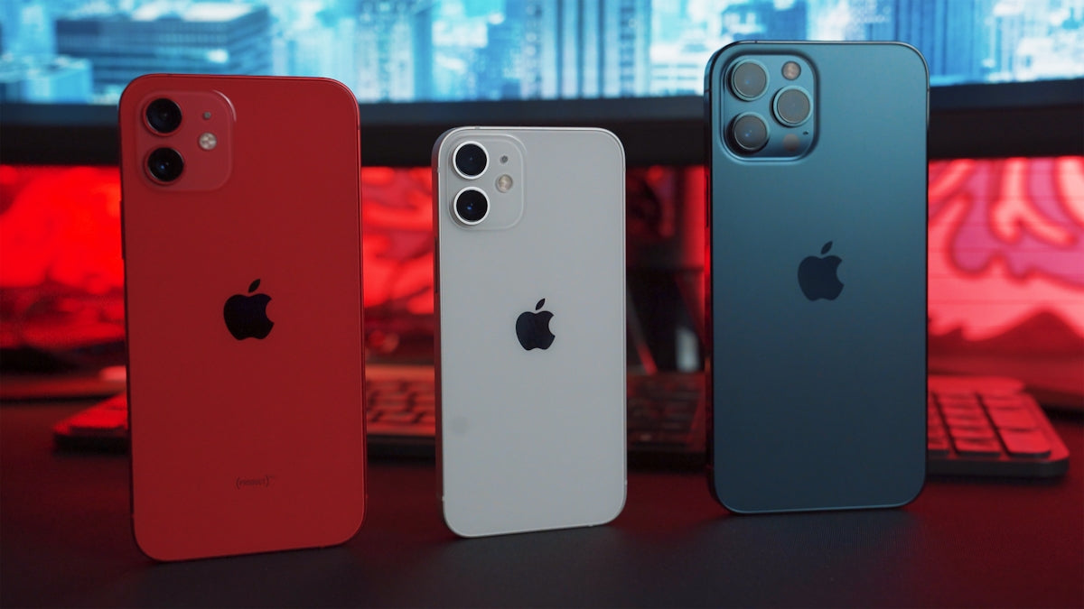 Three modern smartphones in red, white, and blue colors on a desk with a computer background.